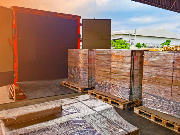 Worker driving forklift loading shipment carton boxes goods on wooden pallet at loading dock from container truck to warehouse cargo storage in freight logistics, transportation industrial, delivery trabajador conduciendo carretilla elevadora de carga cajas de cartón de mercancías en palet de madera en el muelle de carga desde el camión contenedor hasta el almacenamiento de carga de almacén en logística de carga, transporte industrial, entrega