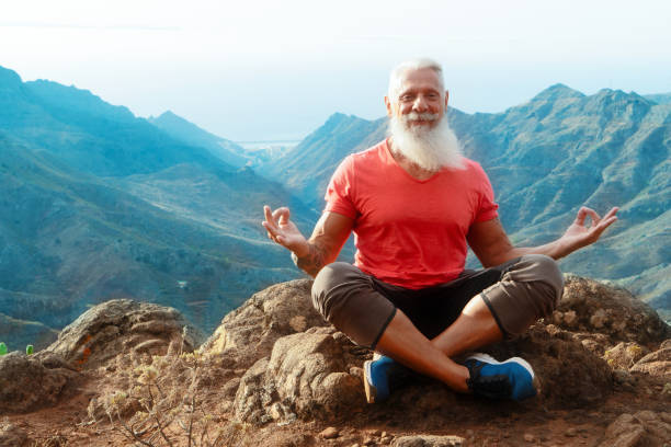 Senior man greeting sunset Senior athlete man with white beard and tattoo greeting sunrise and meditating, mindful living and healthy wellbeing concept man yoga tattoo stock pictures, royalty-free photos & images