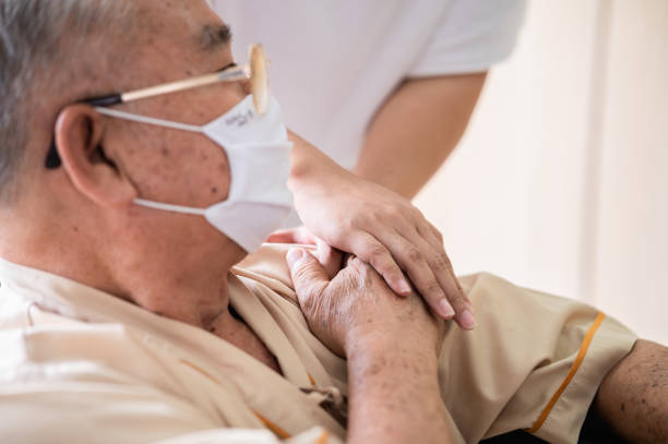 chiudi le mani del medico o della famiglia cugina tenendo con cura le mani del paziente anziano indossando la maschera facciale per prevenire l'infezione da virus in comfort e console durante il recupero in ospedale. - consoling close up senior adult grandparent foto e immagini stock