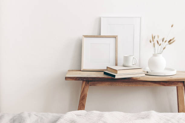istock Portrait and square wooden picture frames mockups. Vintage bench, table with modern ceramic vase, bunny tail dry grass, books and cup of coffee. White wall background. Scandinavian interior. 1272576003