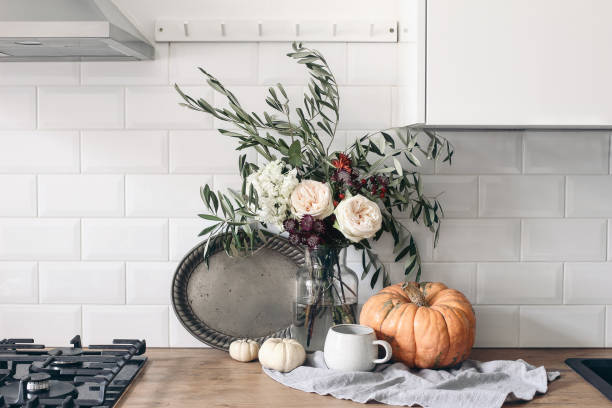 istock Autumn still life composition in rustic eclectic kitchen interior. Cup of coffee, vintage silver tray and floral bouquet. Wooden table background with pumkins. Thanksgiving, Halloween concept. 1272576047