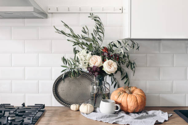 Autumn still life composition in rustic eclectic kitchen interior. Cup of coffee, vintage silver tray and floral bouquet. Wooden table background with pumkins. Thanksgiving, Halloween concept. stock photo