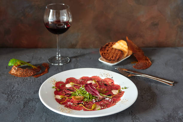 carpaccio de viande dans une plaque blanche sur un fond en bois, avec le pain et le vin délicieux dans un verre - carpaccio red meat caper bread photos et images de collection