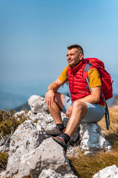 istock Adult man with back pack sitting on a rock in mountains 1272578909