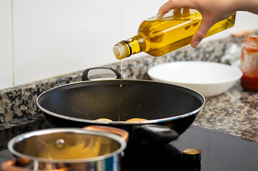 woman pouring cooking oil from bottle into frying pan on stove