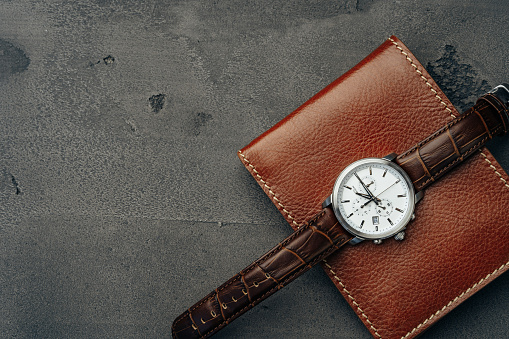 Male watch and leather wallet on dark grey surface close up