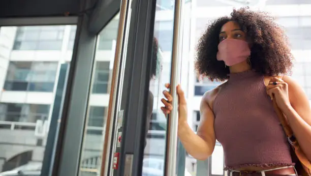 Photo of Young adult woman entering office wearing face mask looking off camera