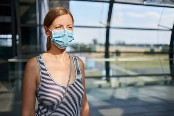 A portrait of a young blonde woman with surgical mask or face mask at the airport, photographed in high resolution with copy space