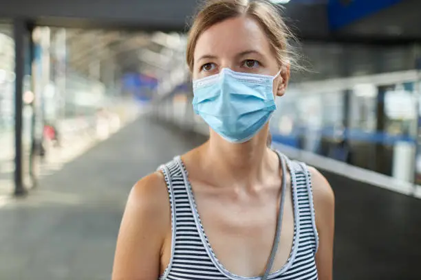 A portrait of a young blonde woman with surgical mask or face mask at the airport, photographed in high resolution with copy space