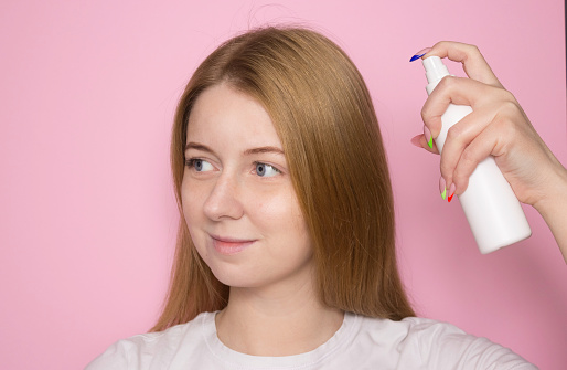 Woman with long hair holds a spray bottle in a white bottle and sprays it on her hair. Hair care product, body care.