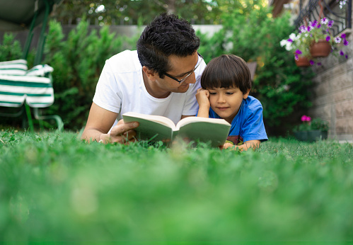 Boy is reading a book with his father in the garden
