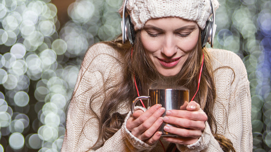 Young woman with headphones and hot tea outdoors winter portrait