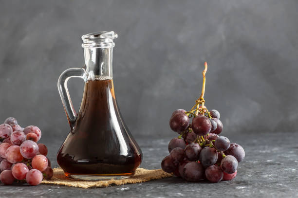 garrafa de vidro de vinagre balsâmico de uva preta orgânica feita de uvas frescas fermentadas. alimentos orgânicos saudáveis frutas negras, foco seletivo - balsamic vinegar vinegar bottle container - fotografias e filmes do acervo