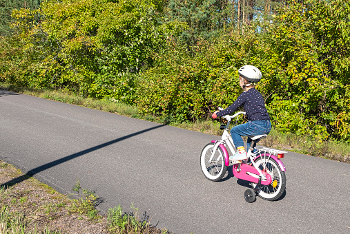 The girl has the first bike. The child is 5 years old. The child learns to drive a bike. Pedestrian and bike path in the suburbs. The real situation. The first experience of a new sport or entertainment.