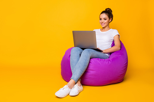 Full body photo of positive cheerful girl sit violet bag armchair use computer, read e-book wear white t-shirt footwear isolated over bright shine color background