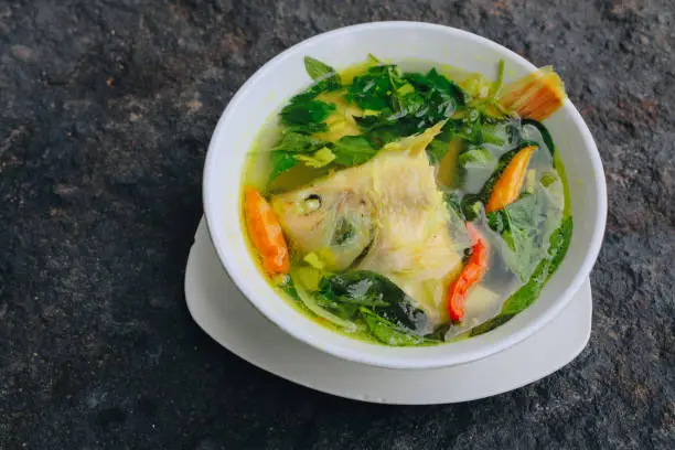Gurame fish head soup or sup kepala ikan gurame with basil leaves, tomatoes, yellow curry, and chilli in a bowl. Indonesian food