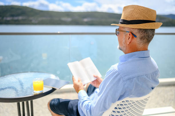 homem maduro curtindo a varanda e lendo um livro - balcony beach book men - fotografias e filmes do acervo