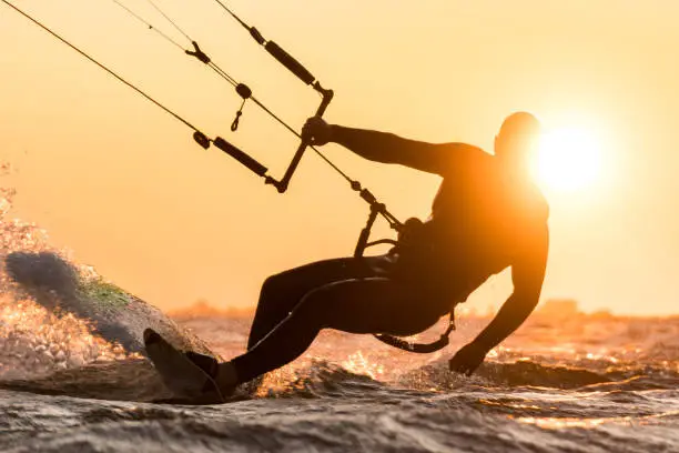 Silhouette of kitesurfer riding in beautiful sunset conditions with sun behind and lens flare