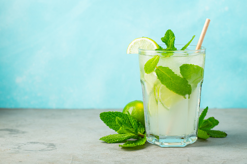 Two homemade lemonade or mojito cocktail with lime, mint and ice cubes in a glass on a light stone table. Fresh summer drink. With copy space