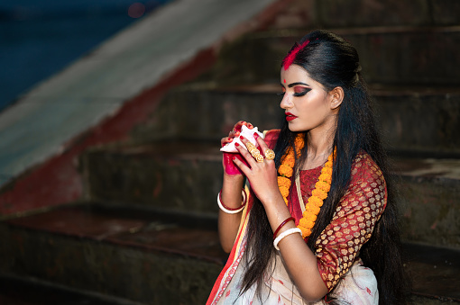 Traditional Bengali woman wearing red and white sari and blowing shankha.