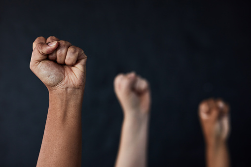Studio shot of a group of women raising their hands in solidarity against a dark background
