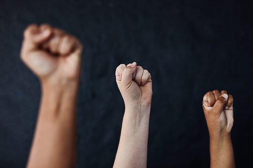 Studio shot of a group of women raising their hands in solidarity against a dark background