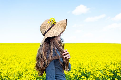 Side view young woman wearing sunhat in field of yellow flowers