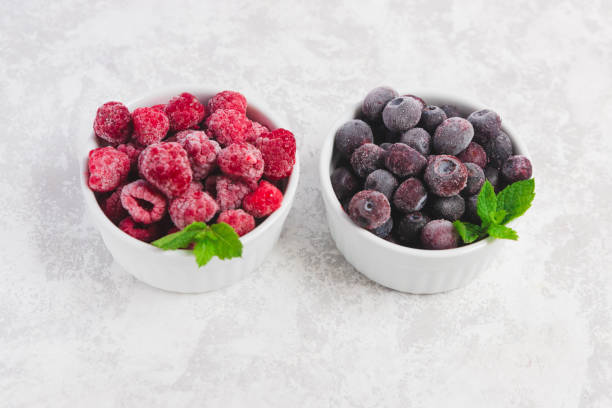 istock Frozen raspberry and blueberries in white bowls on a light concrete background. Procurement of products. Long-term storage. 1272611328