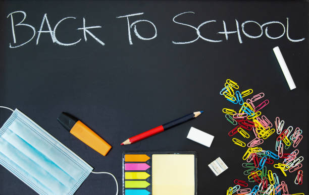 istock Back to school written on a black chalkboard with objects and virus protective mask 1272613881
