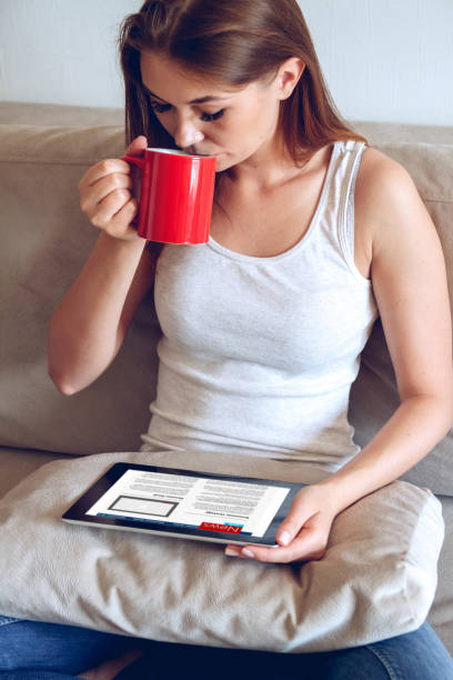 istock Woman sitting on the couch with tablet and coffee in hand 1272616059