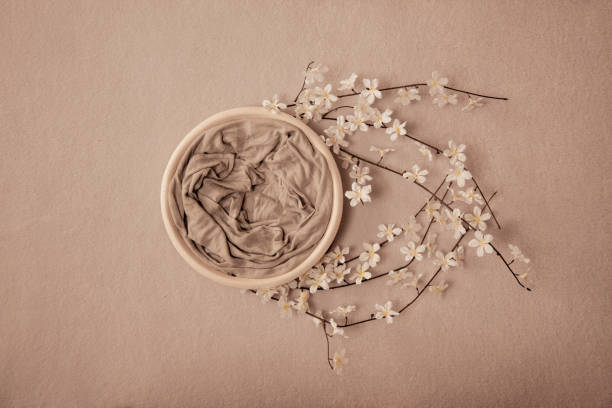 istock Newborn neutral spring background - round white bowl with white flowers and branches wreath on light beige backdrop 1272622273