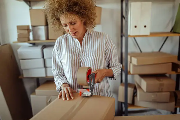 Female entrepreneur packing delivery box at storage warehouse
