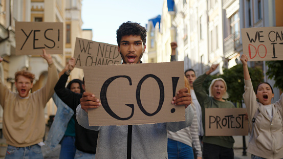 Mixed race man in front of demonstration shows Go poster to protest with activists in background.