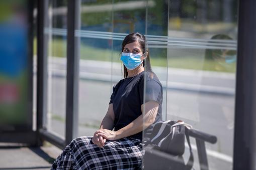 woman with face mask sitting at bus stop