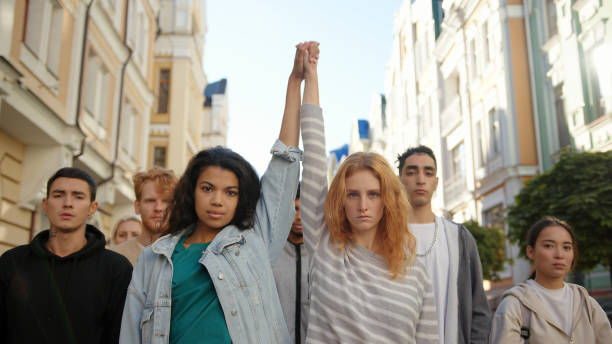 dos mujeres multirraciales cogidos de la mano y levantarlas en protesta masiva contra el racismo - paz mundial fotografías e imágenes de stock