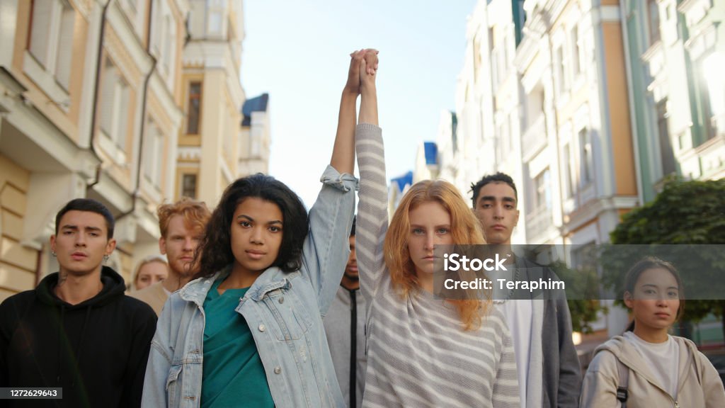 Two multiracial women holding hands together and lift them up in mass protest against racism Two multiracial women holding hands together and lift them up in mass protest against racism. Protest Stock Photo