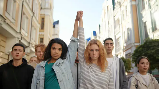 Two multiracial women holding hands together and lift them up in mass protest against racism.