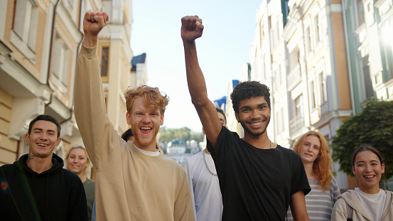 Two happy mixed race men lift hands up together in a mass protest against racism.