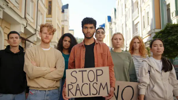 Multiracial students on public demonstration at city street against racism with slogans on posters.