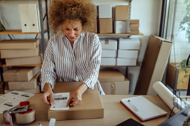 Businesswoman sticking bar code label on delivery package Female entrepreneur labeling delivery package with barcode at distribution warehouse labeling photos stock pictures, royalty-free photos & images
