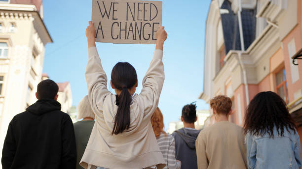 Asian woman in back of protest demonstration holding a poster We need a change. Student activist Asian woman in back of protest demonstration holding a poster We need a change. Student activist. marching photos stock pictures, royalty-free photos & images