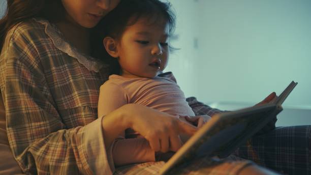 livre asiatique de lecture de mère et de fille à la maison dans la chambre à coucher - baby book toddler reading photos et images de collection
