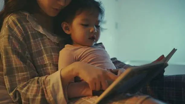 Photo of Asian Mother and daughter reading book at home in the bedroom