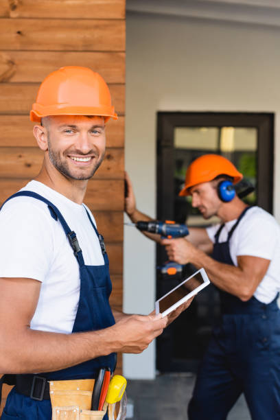 istock Selective focus of builder holding digital tablet near colleague working with electric screwdriver on facade of building 1272638965