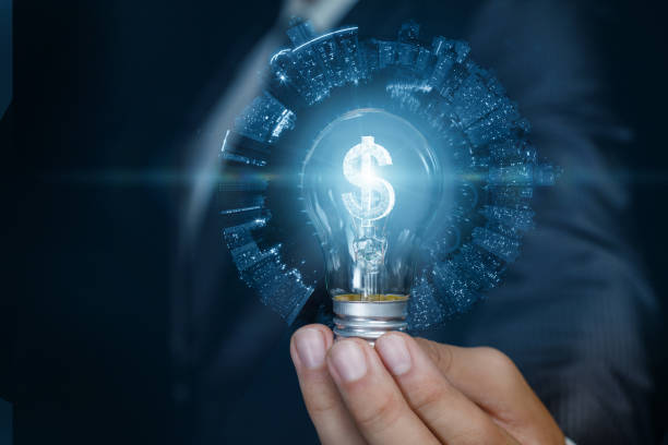 Businessman showing light bulb with burning dollar hologram inside on blue background.