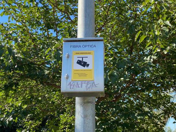 Video surveilled zone Valencia, Spain - September 11, 2020: Box hanging from pole with sign informing about a video surveilled area in the Turia Garden. There are cameras installed along the whole riverbed for security reasons surveillance camera sign stock pictures, royalty-free photos & images