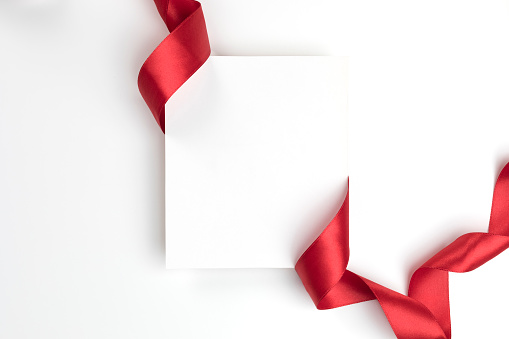 White blank empty card on white background wrapped with a red colored ribbon.