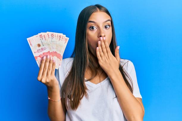 Young hispanic woman holding colombian pesos covering mouth with hand, shocked and afraid for mistake. surprised expression Young hispanic woman holding colombian pesos covering mouth with hand, shocked and afraid for mistake. surprised expression colombian peso stock pictures, royalty-free photos & images