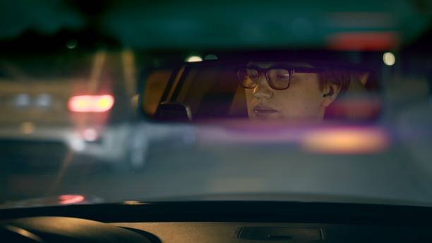 istock Smiling driver's face is reflected in a rear view mirror, night lens flare 1272661873