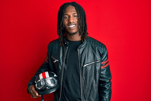 African american man with braids holding motorcycle helmet looking positive and happy standing and smiling with a confident smile showing teeth